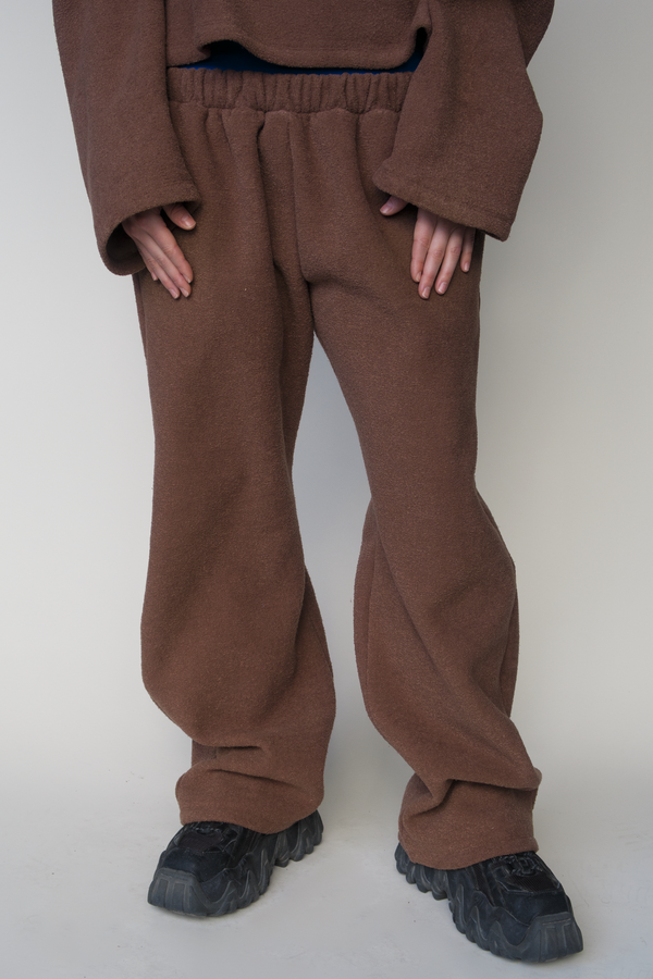 woman standing against beige backdrop wearing a large brown fleece sweater and brown straight-leg, low-rise fleece sweatpants. paired with black sneakers.  