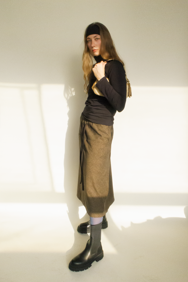 woman standing with black cotton headband, styled with a black turtleneck and brown long skirt and black boots
