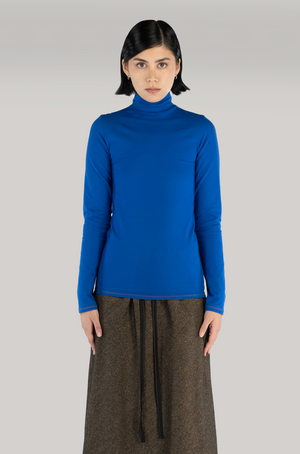 woman standing with cobalt blue turtleneck and long brown wool skirt.