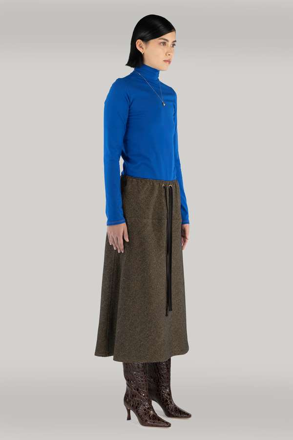 woman standing tall wearing a cobalt blue turtleneck and long brown wool skirt and maroon snake boots