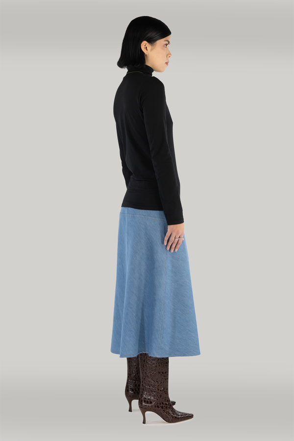 woman standing wearing a black turtleneck and long blue maxi skirt and maroon boots