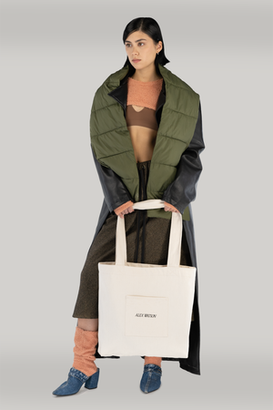 woman standing holding a heavyweight canvas tote bag in her hands. wearing a long coat, cropped sweater showing midriff.