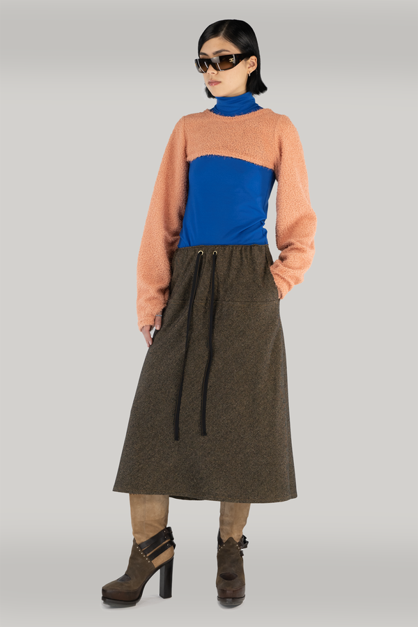 woman standing in front of grey backdrop wearing a cropped orange fuzzy sweater with a cobalt blue turtleneck.  Also wearing a brown maxi wool skirt and brown boots